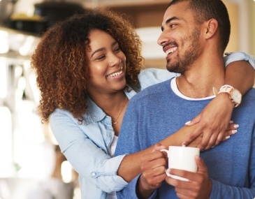 Smiling woman hugging a man holding a white coffee mug