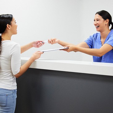 Smiling dental assistant handing patient form