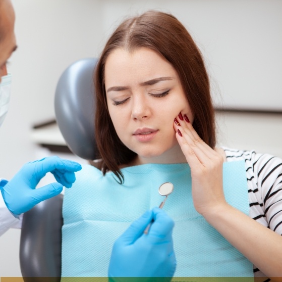 Woman holding her cheek in pain while visiting emergency dentist