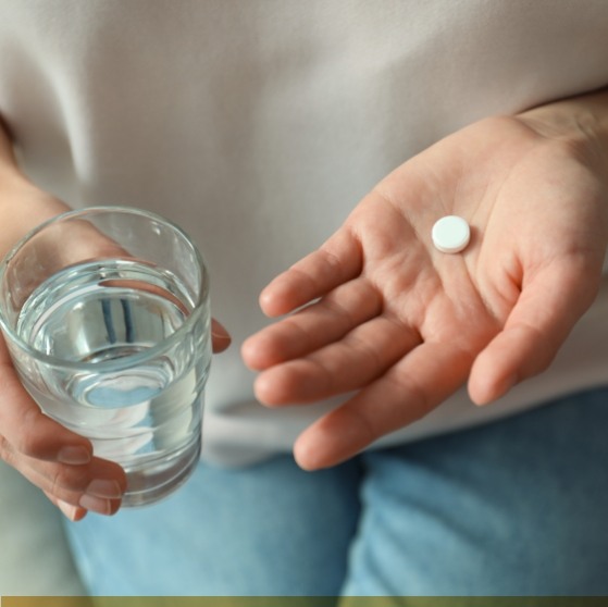 Person holding a pill and a glass of water