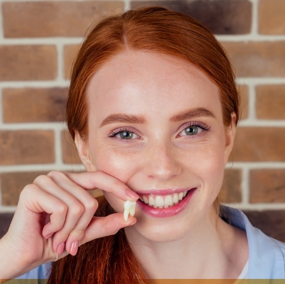 Smiling woman holding a tooth after tooth extractions in Stone Mountain